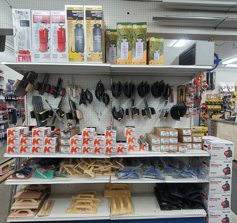 A shelf with cement trowels, industrial and heavy duty lawn sprayers, and contractor garbage bags.