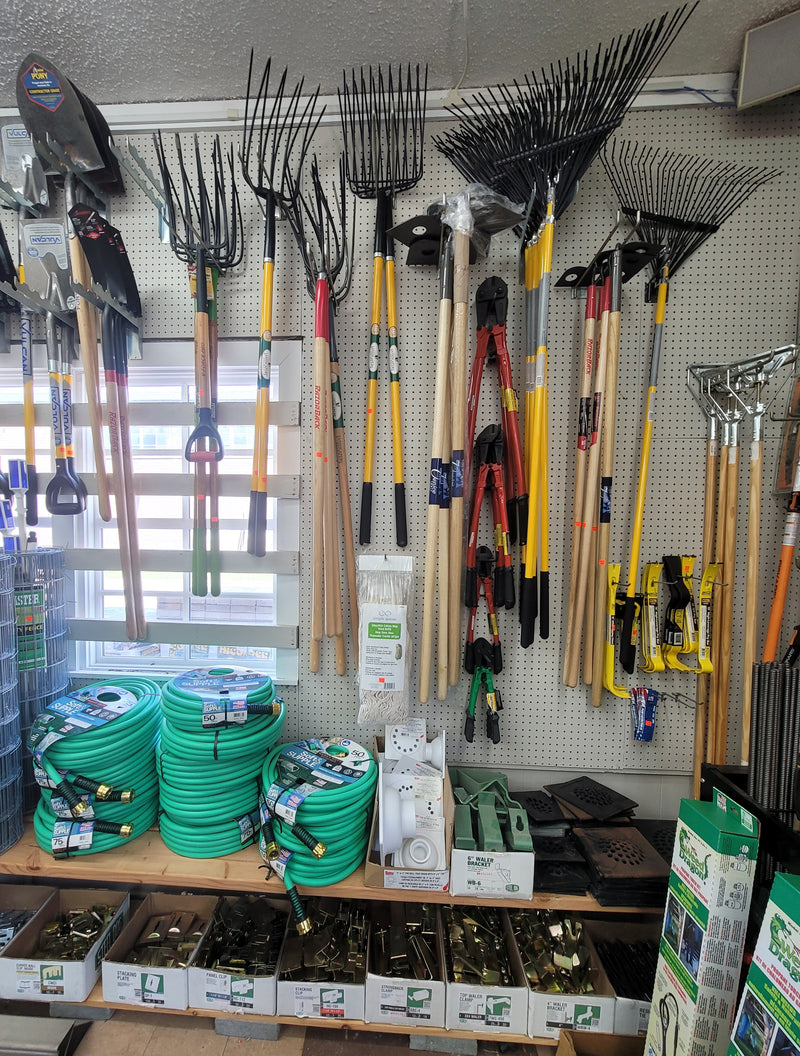 Wall displaying pitchforks, rakes, and garden hoses on a shelf below.